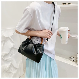Detail of black pleated cloud bag featuring retro round wooden handle and crossbody strap