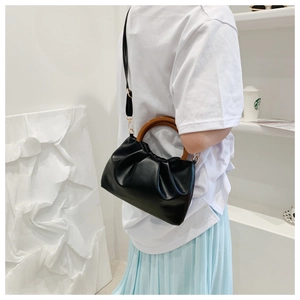 Detail of black pleated cloud bag with wooden handles worn crossbody by model