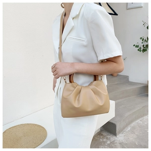 Detail of beige pleated cloud handbag featuring round wooden handles and soft PU leather