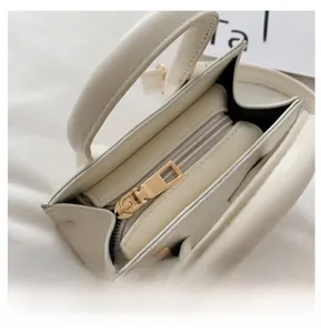Detailed top view of the smooth golden metal zipper closure on the cream PU leather handbag