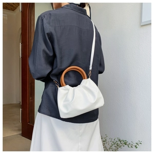 Detail of white pleated cloud bag featuring a circular wooden handle and adjustable strap
