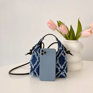 Sac seau en jean bleu matelassé avec franges, présenté à côté d'un smartphone pour taille