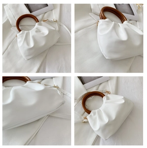 Detail view of white pleated cloud bag with round wood handles and gold hardware accents