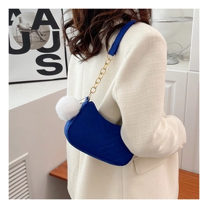 Blue velvet saddle bag with V-shaped quilting and a fluffy white pom-pom detail