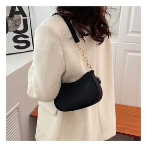 Detail of black quilted shoulder bag with golden chain and plush ball accessory