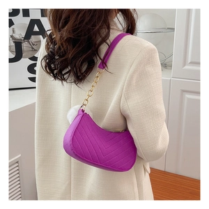 Detail of purple quilted underarm bag with gold chain strap and plush ball pendant