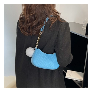 Detail of blue quilted shoulder bag with gold chain strap and white pompom accessory