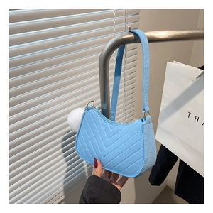 Close-up of light blue hobo bag with V-shaped quilting and a white plush pompom charm