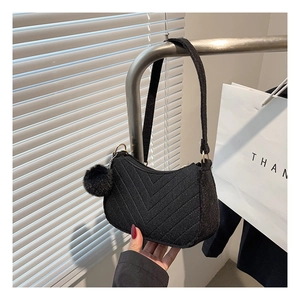Detail of black wool underarm bag with V-shaped quilting and a fluffy pompom keychain
