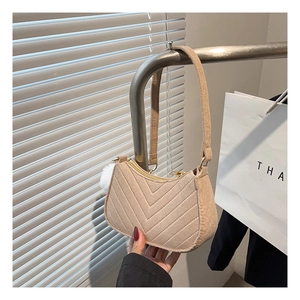 Close-up of beige melon-shaped shoulder bag with V-quilted texture and plush ball charm
