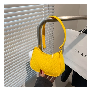 Detail of yellow V-quilted hobo bag with plush ball charm and top zipper closure