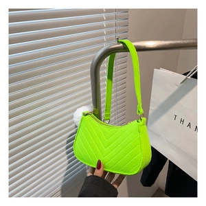 Detail of neon green baguette bag with V-shaped quilting and white fur pompom charm