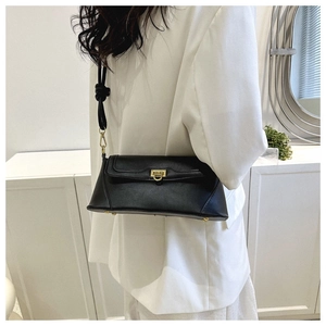 Detail of minimalist black leather baguette bag with gold buckle on white blazer