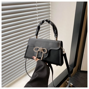 Detail einer schwarzen PU-Handtasche mit Strass-Schleife und gerafftem Griff