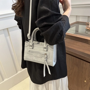 Mini sac bandoulière argenté avec pompon et doubles poignées dans un décor minimaliste