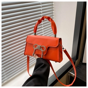 Detail der leuchtend orangefarbenen Handtasche mit Kristallscheife und Plissee-Griff