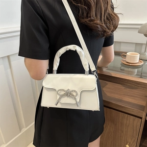 Weiße Kunstledertasche mit glitzernder Schleifenschnalle an Model in schwarzem Kleid