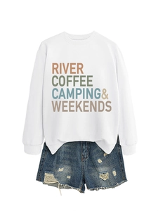 Flat lay detail of a white graphic sweatshirt with River Coffee Camping text and denim shorts