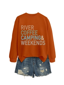 Flat lay of burnt orange sweatshirt with River Coffee Camping print and ripped denim shorts