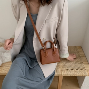 Brown mini square crossbody bag with handle and strap shown on a model in neutral blazer
