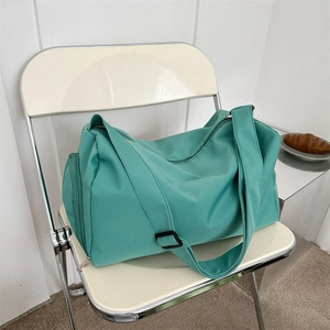 Large mint green nylon travel bag with adjustable strap on a chair in a cozy cafe setting