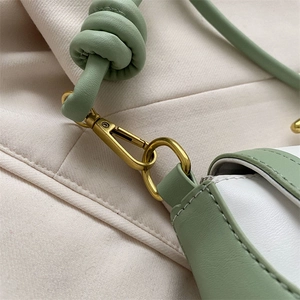 Detail of knotted sage green leather strap and vintage gold metal clasp on baguette bag