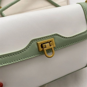 Detail of sage green stitching and golden D-shaped metal lock on white leather bag