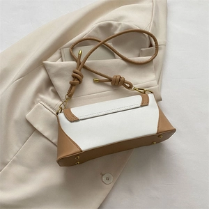 Detail of a minimalist baguette bag with white and camel contrast leather and knotted strap