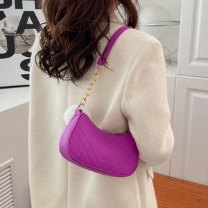 Quilted purple hobo bag with gold chain strap and plush pompom, worn with a beige suit