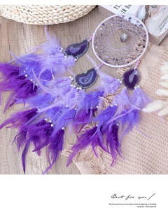 Detailed shot of handmade purple dreamcatcher with agate slices and soft hanging feathers