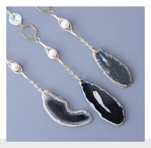 Detail of natural agate stone pendants with gold chains and pearl accents on gray background