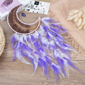 Moon-shaped dream catcher with tree of life crystals and purple feathers on a wooden desk