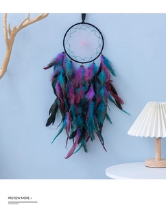 Boho-Traumfänger mit lila und blaugrünen Federn an einer hellblauen Wand hängend