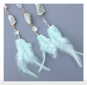 Macro detail of turquoise stone wrapping and light blue feathers on dreamcatcher pendant