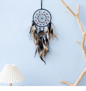 Handgefertigter Boho-Traumfänger mit schwarzen Federn und Achatstein vor blauer Wand im Detail