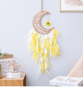 Detail of yellow moon dreamcatcher with feathers and sunflower charm on a gray wall