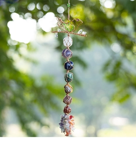 Handcrafted woven bird ornament featuring seven chakra gemstones in a lush garden setting
