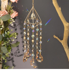 Detail of crystal suncatcher with moon pendant and star beads hanging on a tree branch