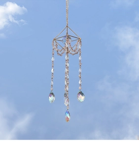 Detail of crystal suncatcher with golden geometric frame and iridescent beads against sky