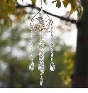 Close-up of geometric crystal suncatcher with rainbow prisms and golden frame hanging outdoors