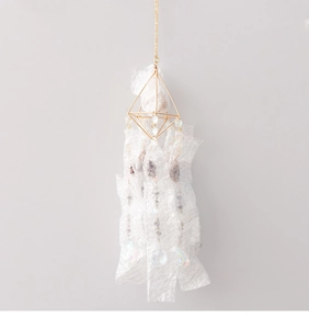 Detail of hanging crystal suncatcher with golden geometric frame and translucent fabric