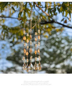 Detailed handmade citrine prism suncatcher with golden frame hanging from a tree branch