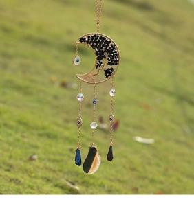 Detail of moon suncatcher with tree of life, agate slice, and evil eye charm in garden