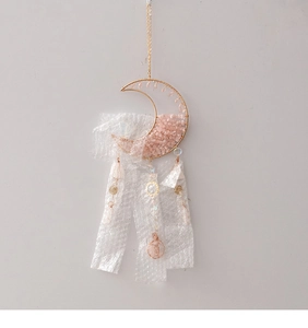 Detail of moon-shaped suncatcher with pink raw stones and handmade golden wire wrapping