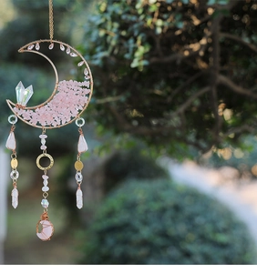 Detail of moon-shaped suncatcher with pink crystals and gold frame hanging in a garden