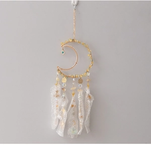 Detail of moon-shaped dreamcatcher with gold metal frame, yellow stones, and evil eye charm