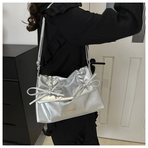 Detail der silbernen Metallic-PU-Schultertasche mit zwei Schleifen und goldenem Logo