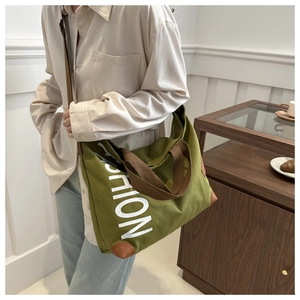 Detailed side view of large green canvas tote bag with brown straps and leather corners