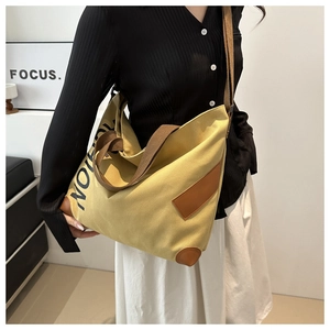 Detail of yellow canvas tote bag with reinforced leather base and shoulder strap