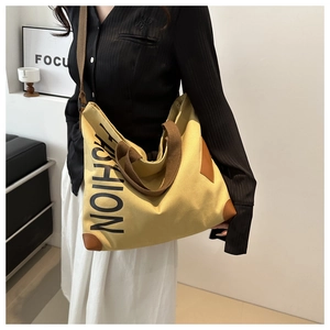 Detail of canvas tote bag with brown leather corners and bold Fashion lettering